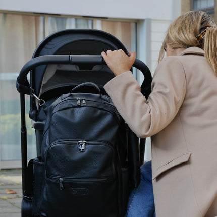 Person looking towards her baby in a stroller with a black changing backpack hanging on via the stroller clips.