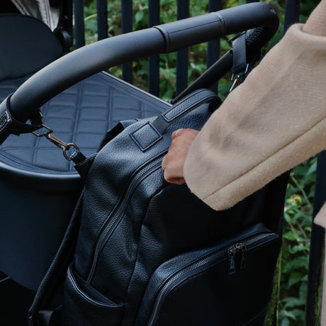 Changing Backpack attached to a pram via pram clips being accessed by a woman.